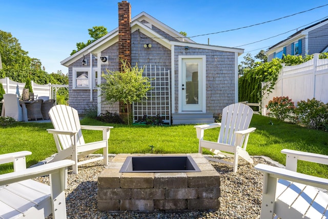 back of house with an outdoor fire pit and a lawn