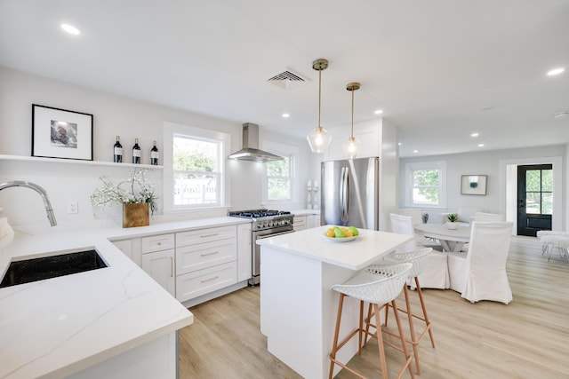 kitchen with white cabinetry, wall chimney range hood, decorative light fixtures, sink, and stainless steel appliances