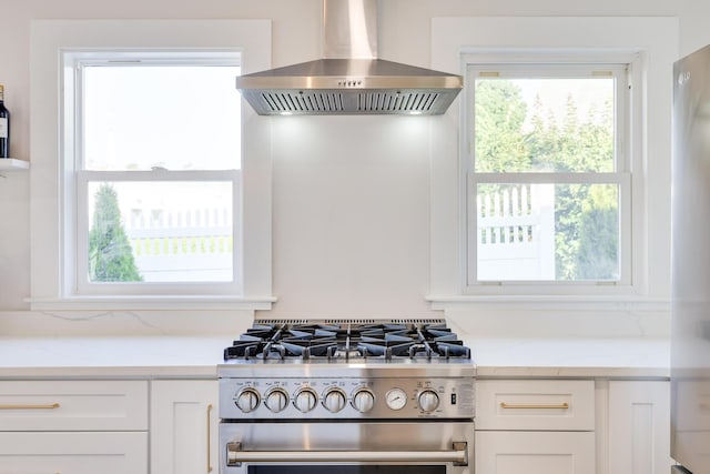 kitchen with light stone countertops, stainless steel range, white cabinetry, and exhaust hood