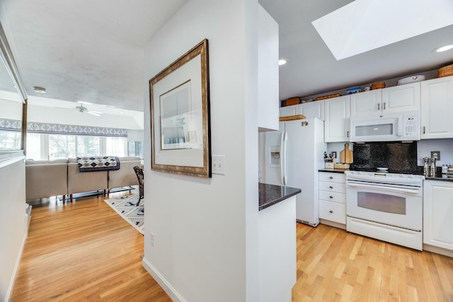 kitchen with white appliances, light hardwood / wood-style flooring, ceiling fan, a skylight, and white cabinets