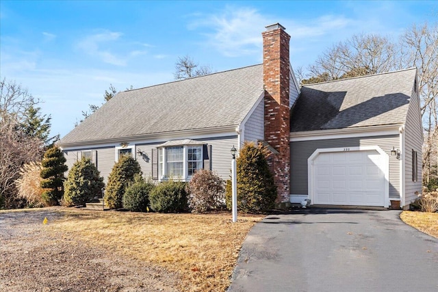 view of front of home with aphalt driveway, a garage, roof with shingles, a chimney, and a front yard