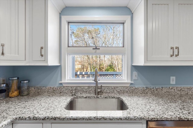 kitchen with white cabinetry, a sink, stainless steel dishwasher, and light stone countertops