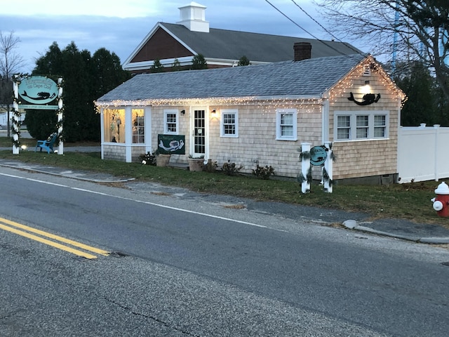 view of front of home featuring a shingled roof, fence, and a chimney