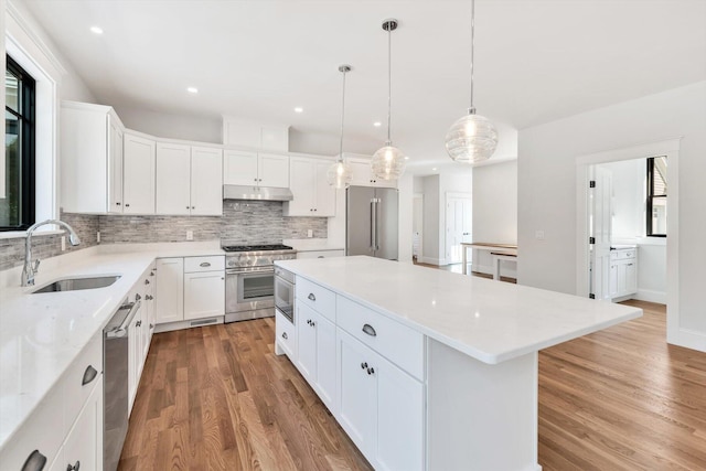 kitchen with premium appliances, sink, a kitchen island, white cabinets, and decorative light fixtures