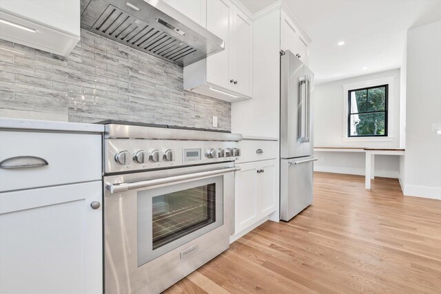 kitchen featuring white cabinetry, wall chimney range hood, tasteful backsplash, light wood-type flooring, and high quality appliances