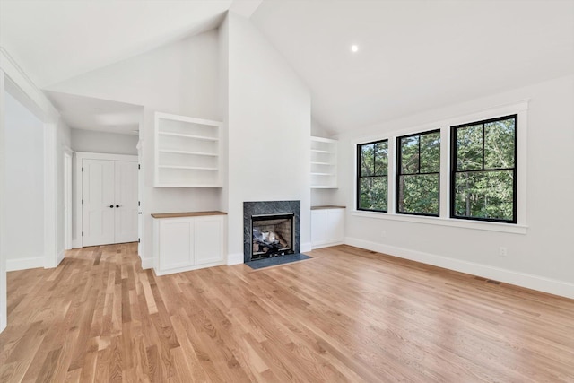 unfurnished living room with built in features, light wood-type flooring, high vaulted ceiling, and a fireplace