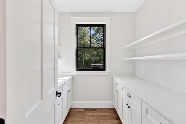 bar featuring light stone counters, white cabinetry, and hardwood / wood-style floors