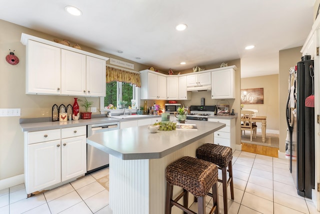 5 Bayes Hill Cir, Oak Bluffs, MA 02557 - kitchen featuring appliances with stainless steel finishes, under cabinet range hood, a kitchen breakfast bar, light tile patterned floors, and white cabinetry