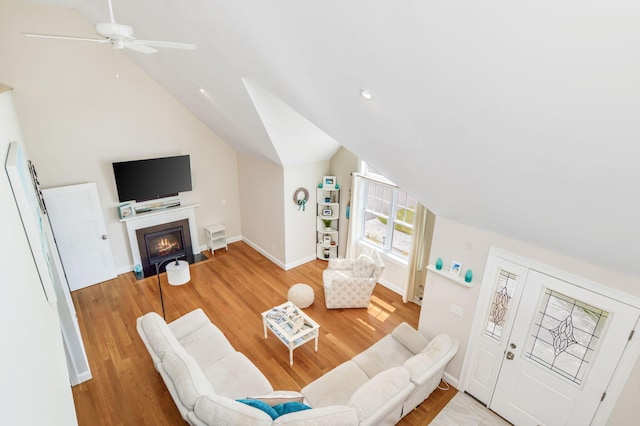 living room featuring lofted ceiling, a ceiling fan, baseboards, a fireplace with flush hearth, and light wood-style floors