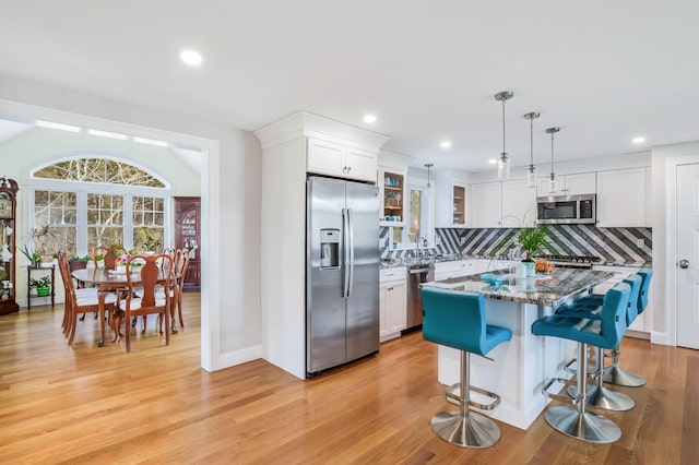 kitchen featuring a breakfast bar area, white cabinets, light wood-style floors, stainless steel appliances, and tasteful backsplash