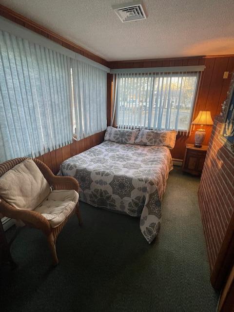 bedroom featuring wooden walls, carpet flooring, and a textured ceiling