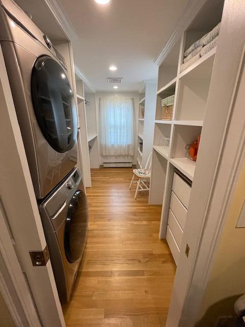 clothes washing area featuring ornamental molding, stacked washing maching and dryer, and light hardwood / wood-style floors