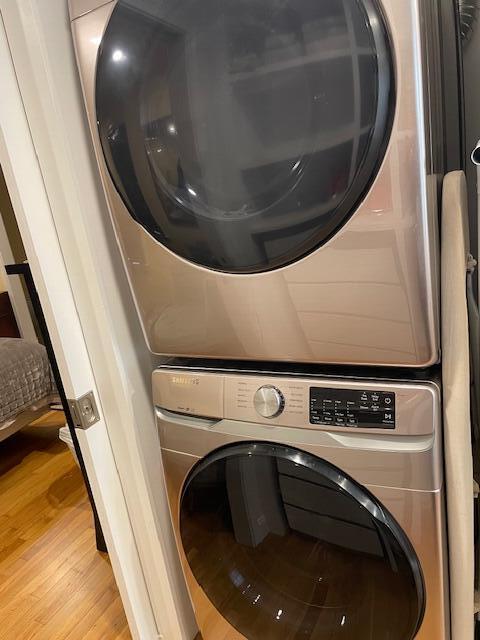 laundry area with stacked washer / drying machine and light hardwood / wood-style floors