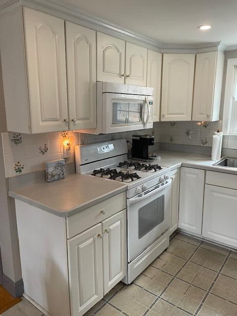 kitchen featuring white cabinetry, backsplash, and white appliances