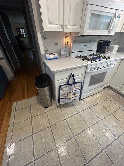 kitchen with light hardwood / wood-style floors, white cabinets, white appliances, and decorative backsplash