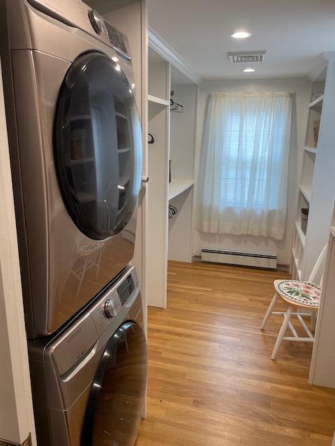 clothes washing area with stacked washer / dryer, a baseboard radiator, and light hardwood / wood-style floors