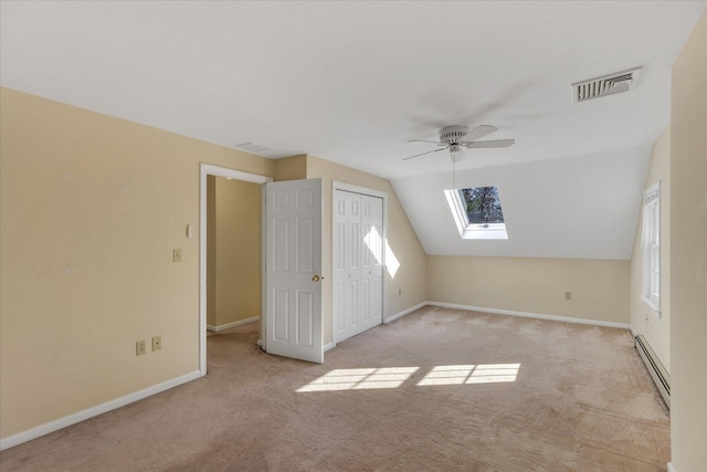 additional living space with light carpet, baseboard heating, vaulted ceiling with skylight, and ceiling fan