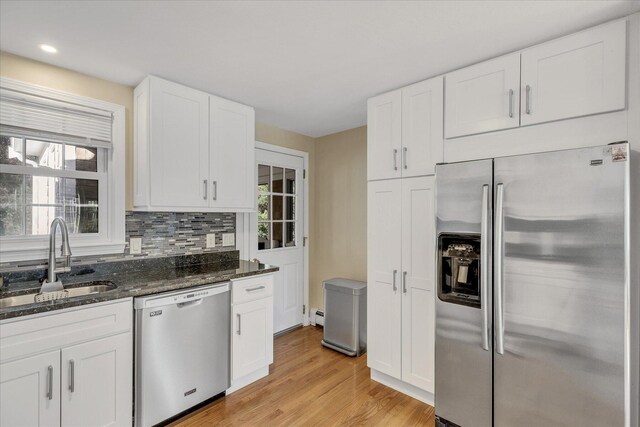 kitchen with appliances with stainless steel finishes, sink, backsplash, white cabinetry, and light wood-type flooring