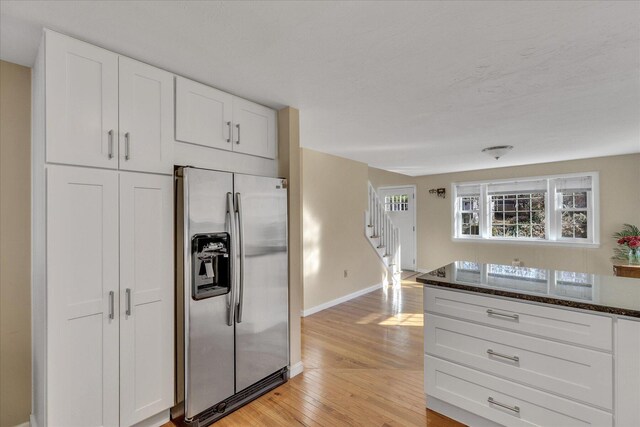 kitchen with stainless steel refrigerator with ice dispenser, white cabinets, light wood-type flooring, and dark stone countertops