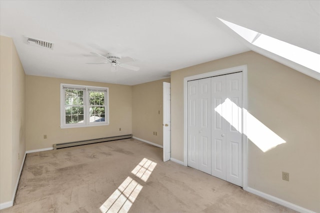 unfurnished bedroom with a baseboard radiator, light carpet, a closet, lofted ceiling with skylight, and ceiling fan