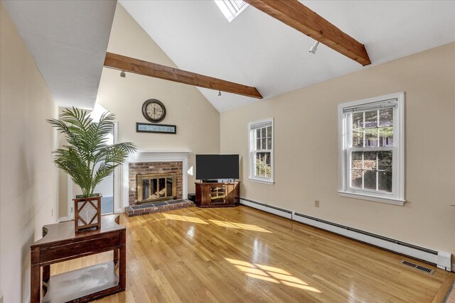 living room with hardwood / wood-style flooring, a brick fireplace, baseboard heating, and vaulted ceiling with skylight