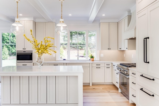 kitchen with a sink, light countertops, appliances with stainless steel finishes, light wood-style floors, and beam ceiling