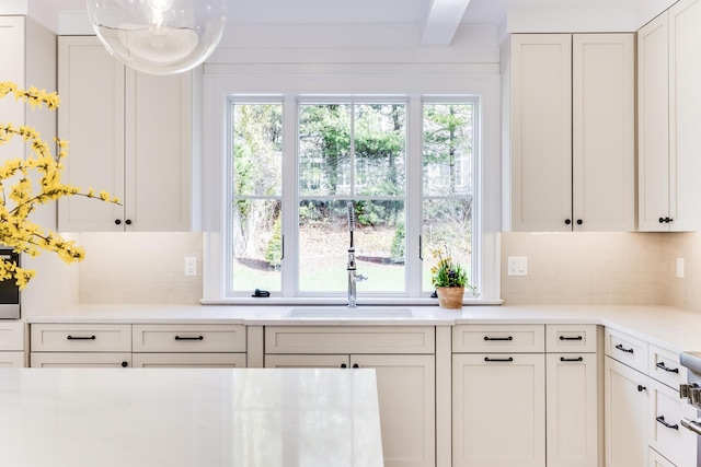 kitchen featuring tasteful backsplash, light countertops, white cabinetry, beamed ceiling, and a sink