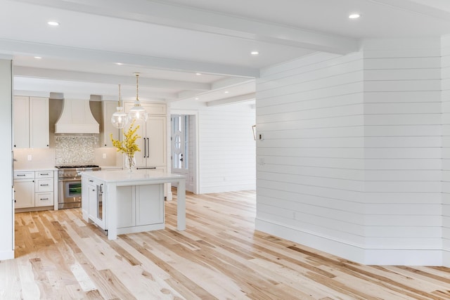 kitchen with stainless steel stove, premium range hood, light countertops, beam ceiling, and decorative backsplash