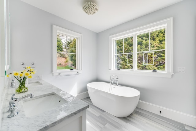 full bathroom with a soaking tub, a healthy amount of sunlight, a sink, and baseboards
