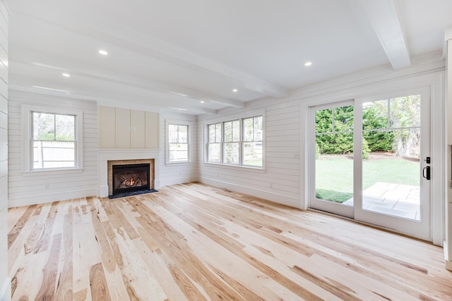 unfurnished living room featuring beam ceiling, light wood-type flooring, a fireplace with flush hearth, and a healthy amount of sunlight
