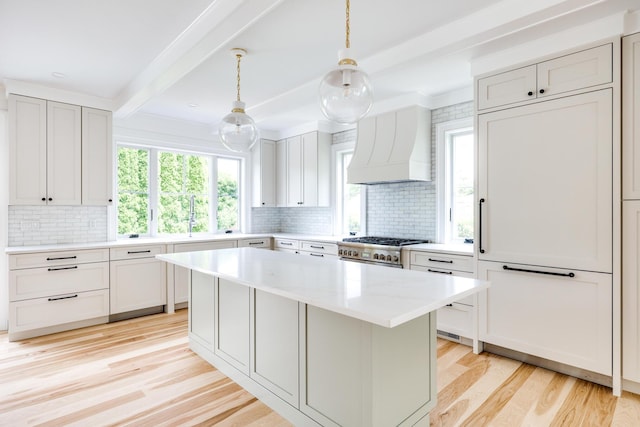 kitchen featuring premium range hood, range, decorative light fixtures, a kitchen island, and beam ceiling