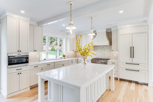 kitchen with custom exhaust hood, backsplash, light wood-style floors, stainless steel range, and a sink