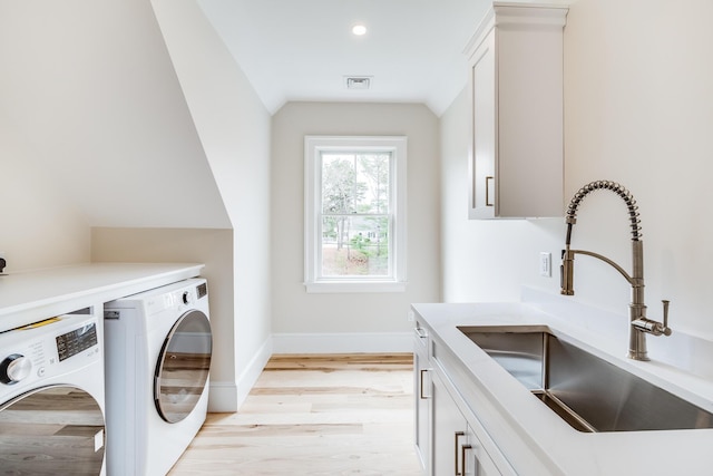 washroom featuring independent washer and dryer, light wood-type flooring, visible vents, a sink, and cabinet space