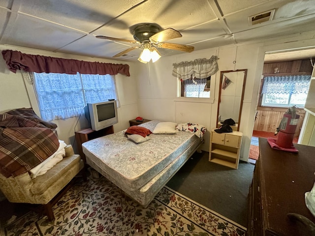 bedroom featuring carpet, wooden walls, visible vents, and ceiling fan