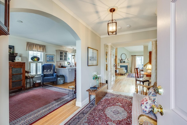 foyer entrance featuring decorative columns, a fireplace, ornamental molding, and wood finished floors