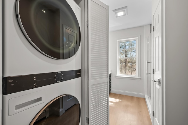 washroom with baseboards, laundry area, stacked washing maching and dryer, and light wood-style flooring