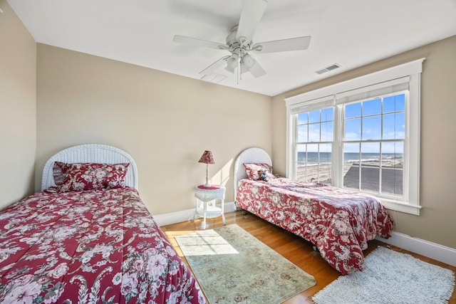 bedroom with ceiling fan, wood-type flooring, and a water view