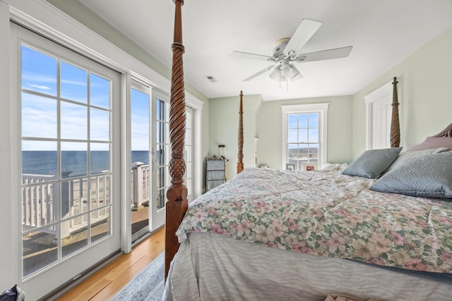 bedroom featuring light hardwood / wood-style floors, a water view, ceiling fan, and access to outside