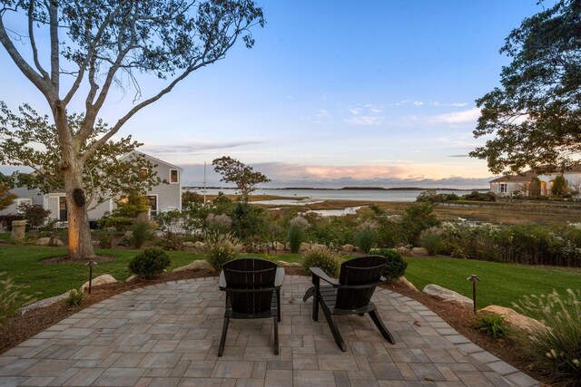 patio terrace at dusk with a water view and a lawn