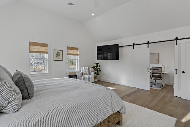 bedroom with vaulted ceiling, a barn door, and light wood-type flooring