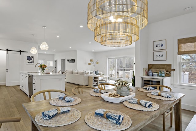 dining room featuring light wood finished floors, a notable chandelier, a healthy amount of sunlight, and a barn door