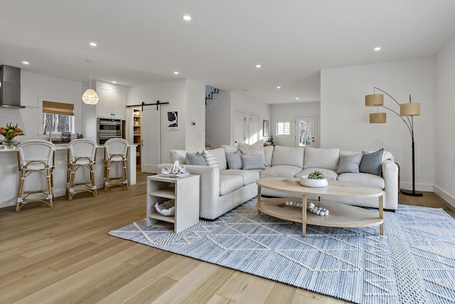 living room featuring recessed lighting, a barn door, baseboards, and light wood finished floors