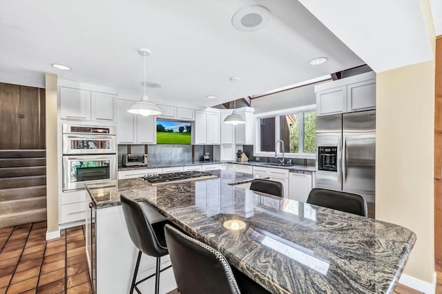 kitchen featuring appliances with stainless steel finishes, decorative light fixtures, sink, dark stone counters, and a kitchen bar