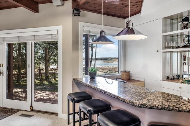 kitchen featuring wood ceiling, beam ceiling, pendant lighting, a breakfast bar, and dark stone counters