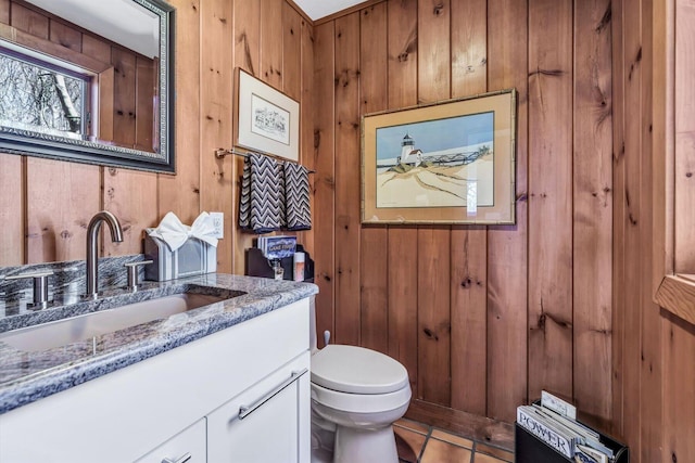 bathroom with toilet, wooden walls, tile patterned floors, and vanity