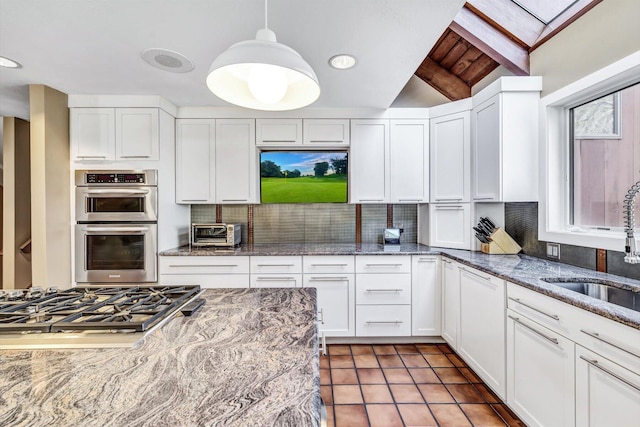 kitchen with stainless steel appliances, decorative light fixtures, white cabinetry, and lofted ceiling with beams