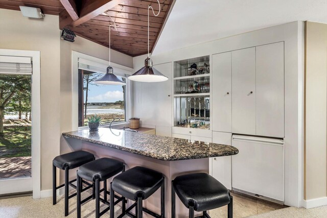 kitchen with pendant lighting, wood ceiling, white cabinetry, dark stone counters, and a kitchen breakfast bar