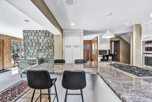 kitchen featuring appliances with stainless steel finishes, decorative light fixtures, white cabinets, dark stone countertops, and wooden walls