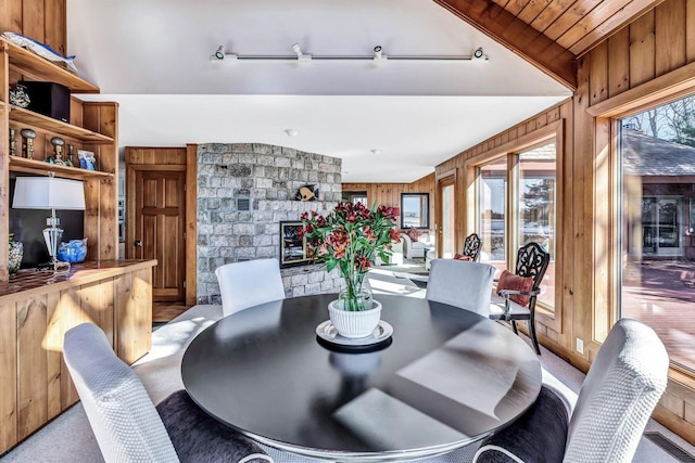 carpeted dining area with lofted ceiling, wood walls, wooden ceiling, and a stone fireplace