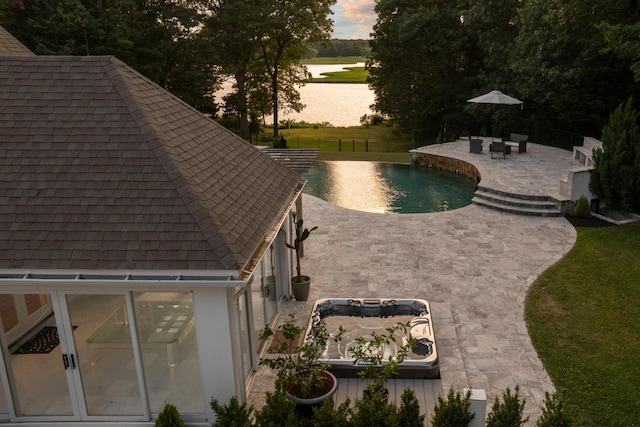 pool at dusk featuring a patio and a hot tub